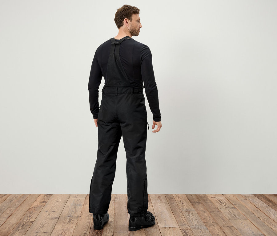 Mann von hinten trägt eine schwarze Skihose mit Hosenträgern und schwarze Skischuhe.