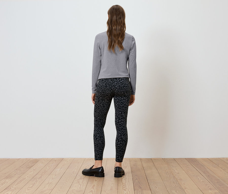 Frau steht mit dem Rücken zur Kamera und trägt ein graues Langarmshirt und schwarze Leggings.