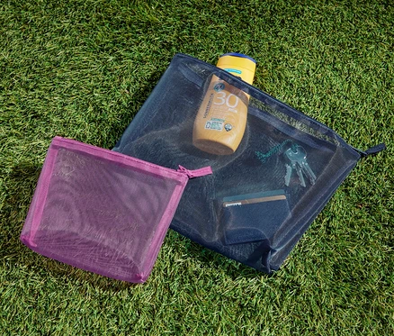 Zwei Aufbewahrungstäschchen liegen auf dem Gras. In einem davon befinden sich Sonnencreme, Schlüssel und eine Karte.