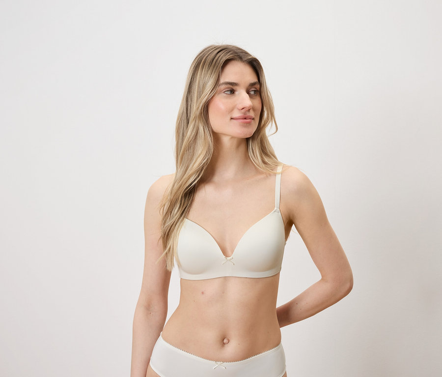Frau mit blonden Haaren und heller Haut posiert in einem hellen BH und Höschen.