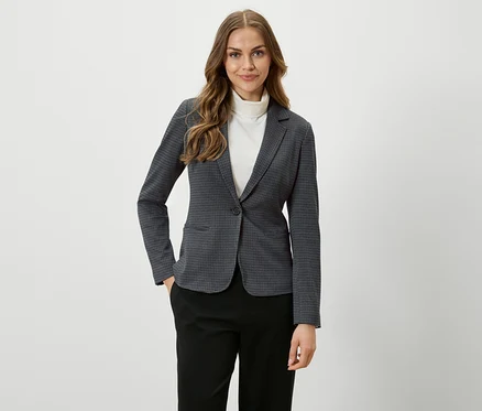 Frau mit braunen Haaren trägt einen karierten Blazer und schwarze Hosen.