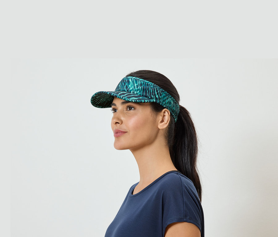 Frau mit Pferdeschwanz und blauem T-Shirt, trägt ein grünes Visor mit Blattmuster.