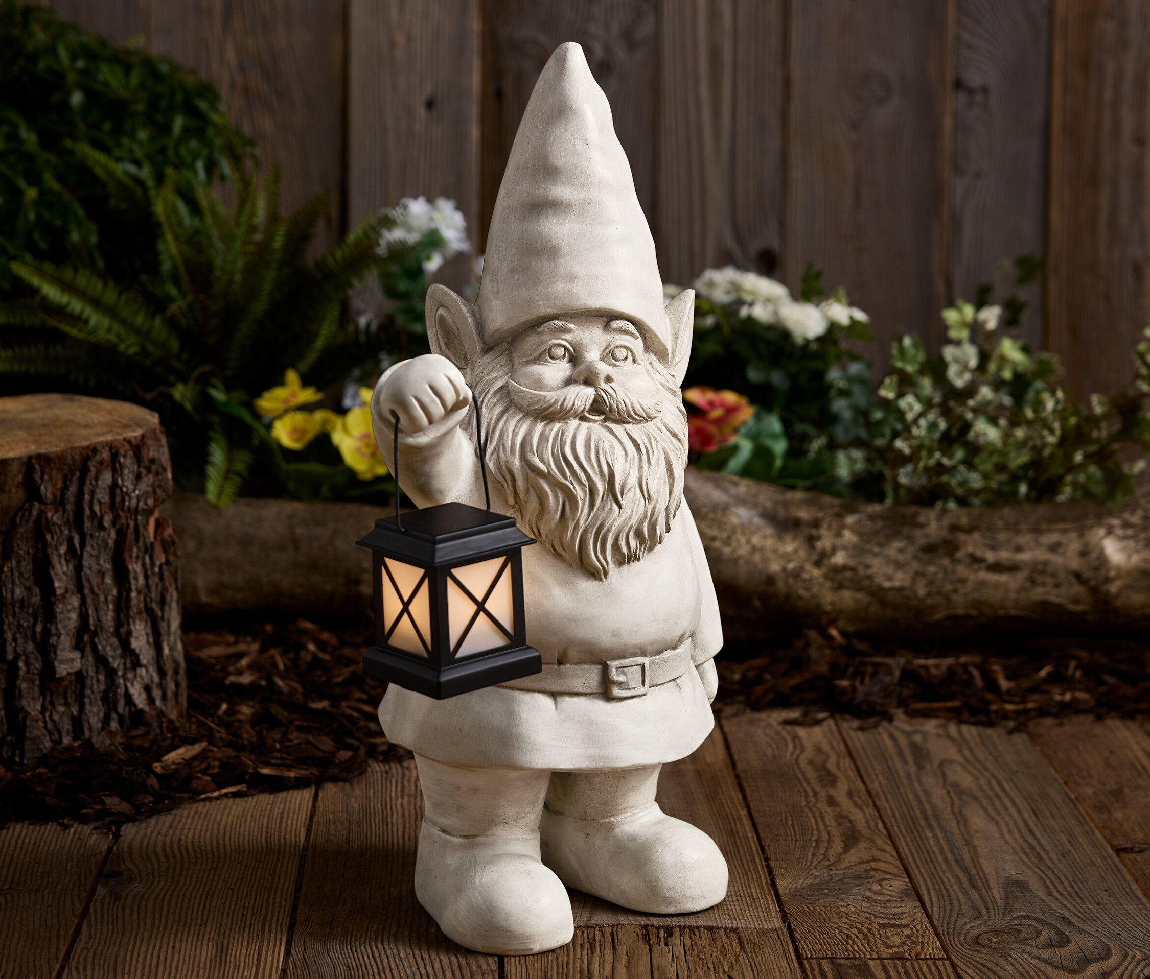 Ein Gartenzwerg aus Stein hält eine schwarze Laterne vor einem Holzhintergrund.