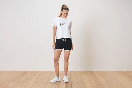 Frau steht in einem weißen T-Shirt mit der Aufschrift LOVE und schwarzen Shorts mit weißen Akzenten.