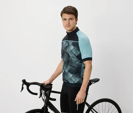 Mann im Radtrikot mit blaugrünen Ärmeln, der ein schwarzes Fahrrad hält.