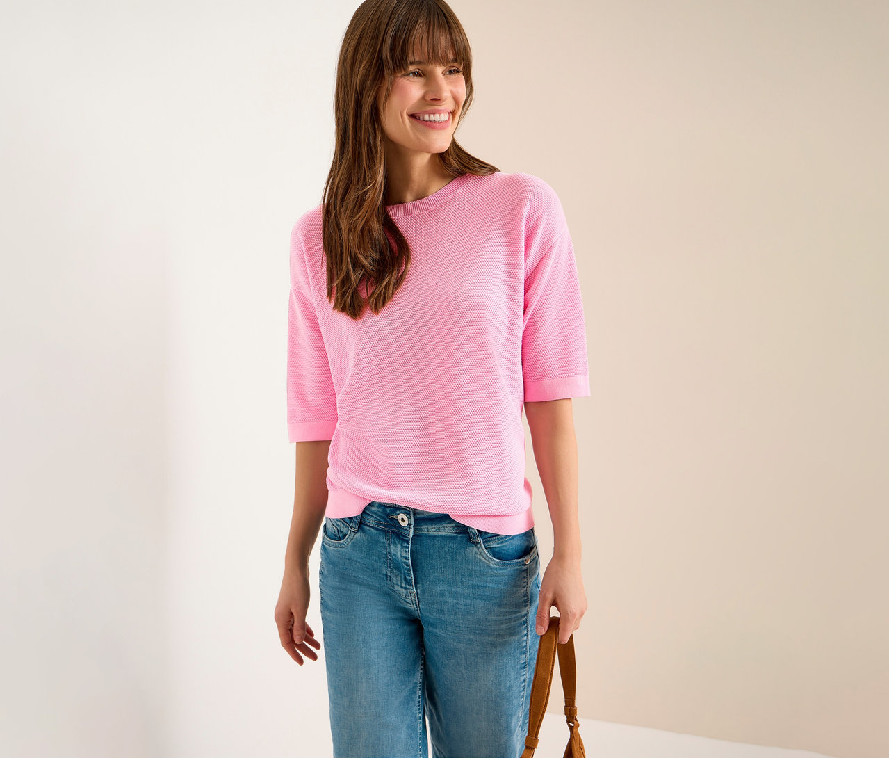 Frau mit Jeans und rosa CECIL Kurzarmpullover, dazu eine braune Handtasche.