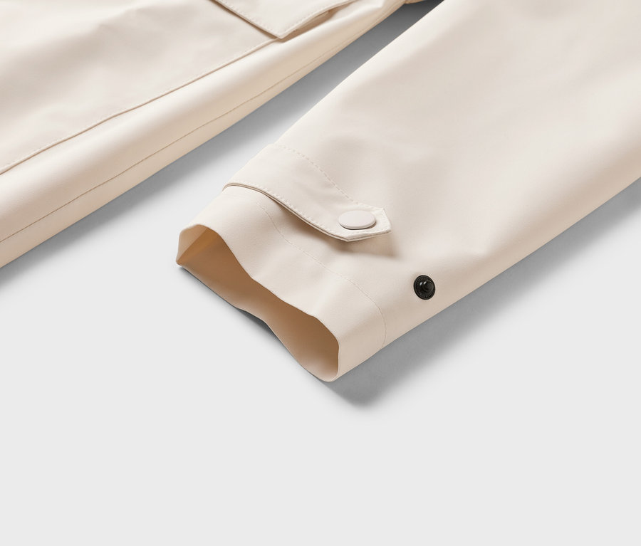 Nahaufnahme eines beigen Jackenärmels mit Knopfdetail und einer Tasche im Hintergrund.