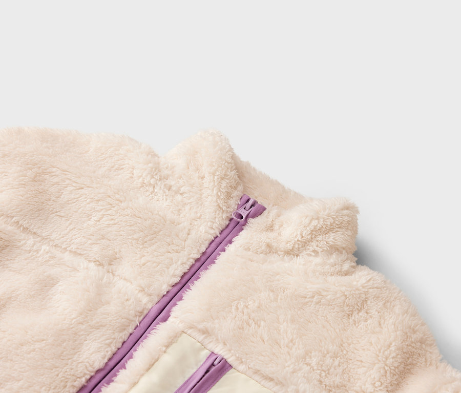 Nahaufnahme einer cremefarbenen Fleecejacke mit lila Reißverschluss.