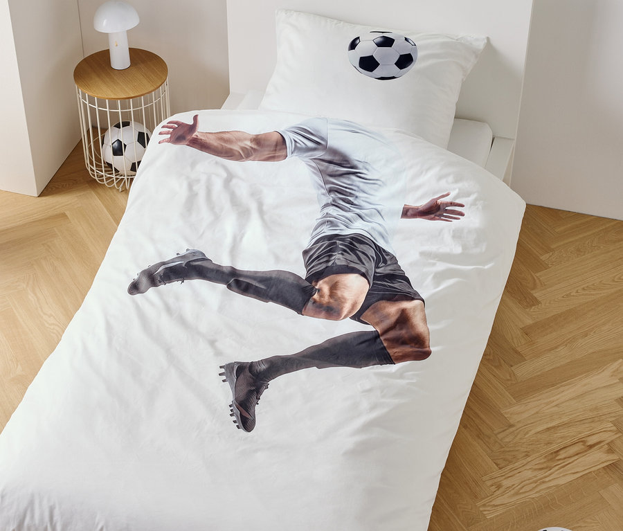 Auf einem Bettbezug ist ein Fußballspieler im Sprung abgebildet, daneben ein Nachttisch mit Lampe und Fußball.