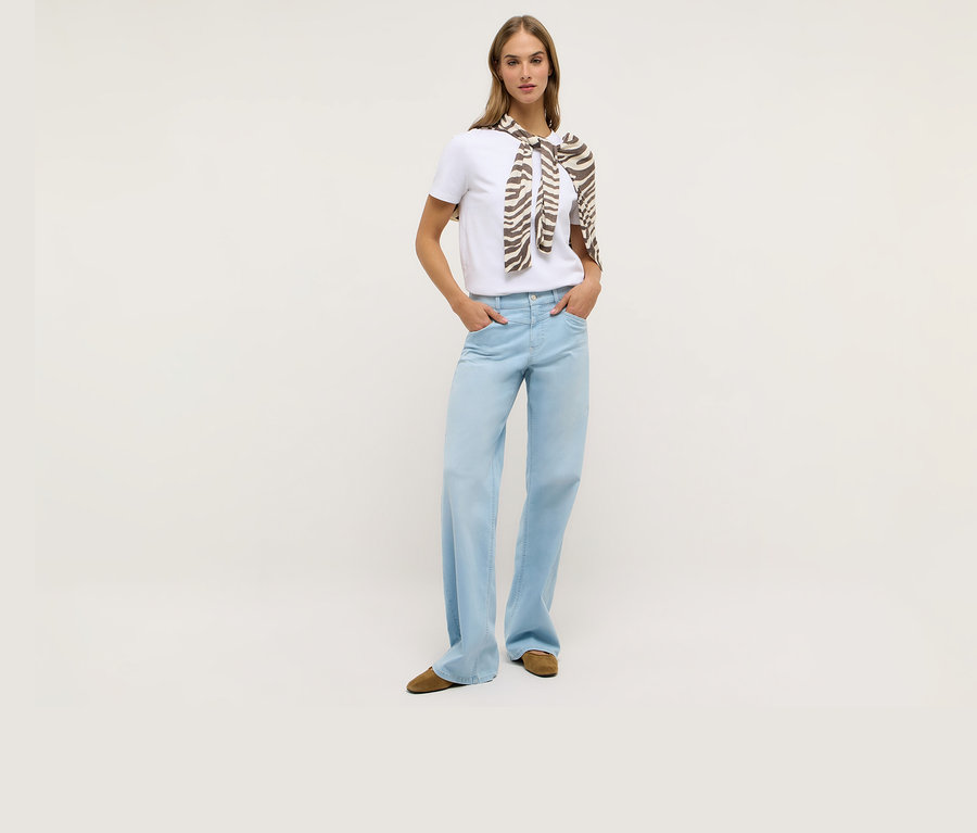 Frau mit weißem T-Shirt und Angels Denim »Liz Modern« Wide Leg Jeans. Ein Schal mit Zebramuster ist um ihre Schultern gebunden.