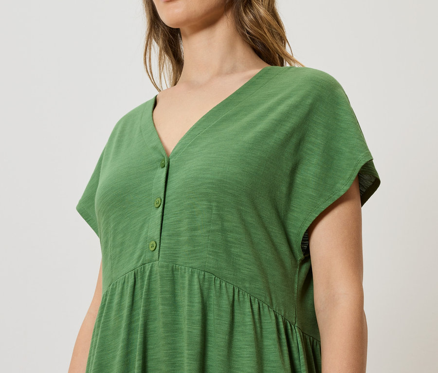 Nahaufnahme einer Frau, die ein grünes Kleid mit Knöpfen trägt.