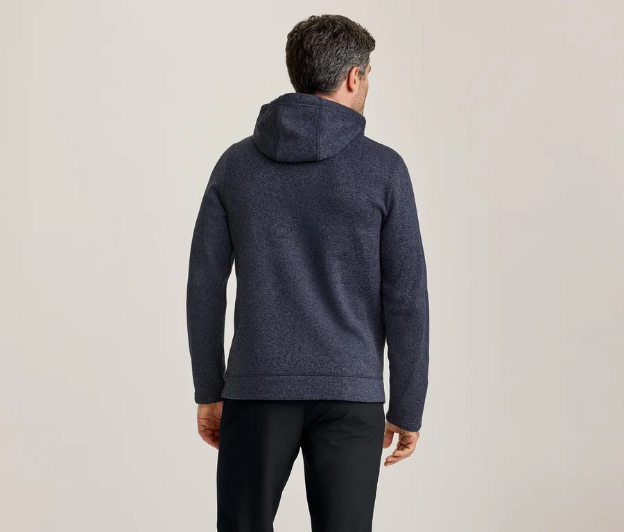 Mann von hinten gesehen, trägt einen dunkelblauen, strukturierten Kapuzenpullover und schwarze Hosen.