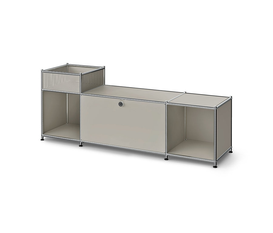 Niedriges, modulares Möbelstück mit Metallrahmen und hellgrauen Paneelen. Links ein perforierter Korb über einem offenen Fach, mittig ein geschlossener Schrank, rechts ein offenes Fach.