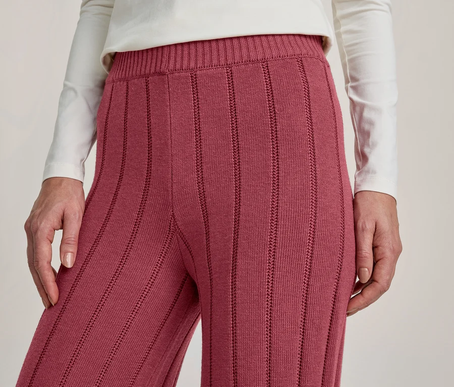 Nahaufnahme einer Person in einem weißen Langarmshirt und einer beerenfarbenen gerippten Strickhose. Die Hände liegen an den Seiten.