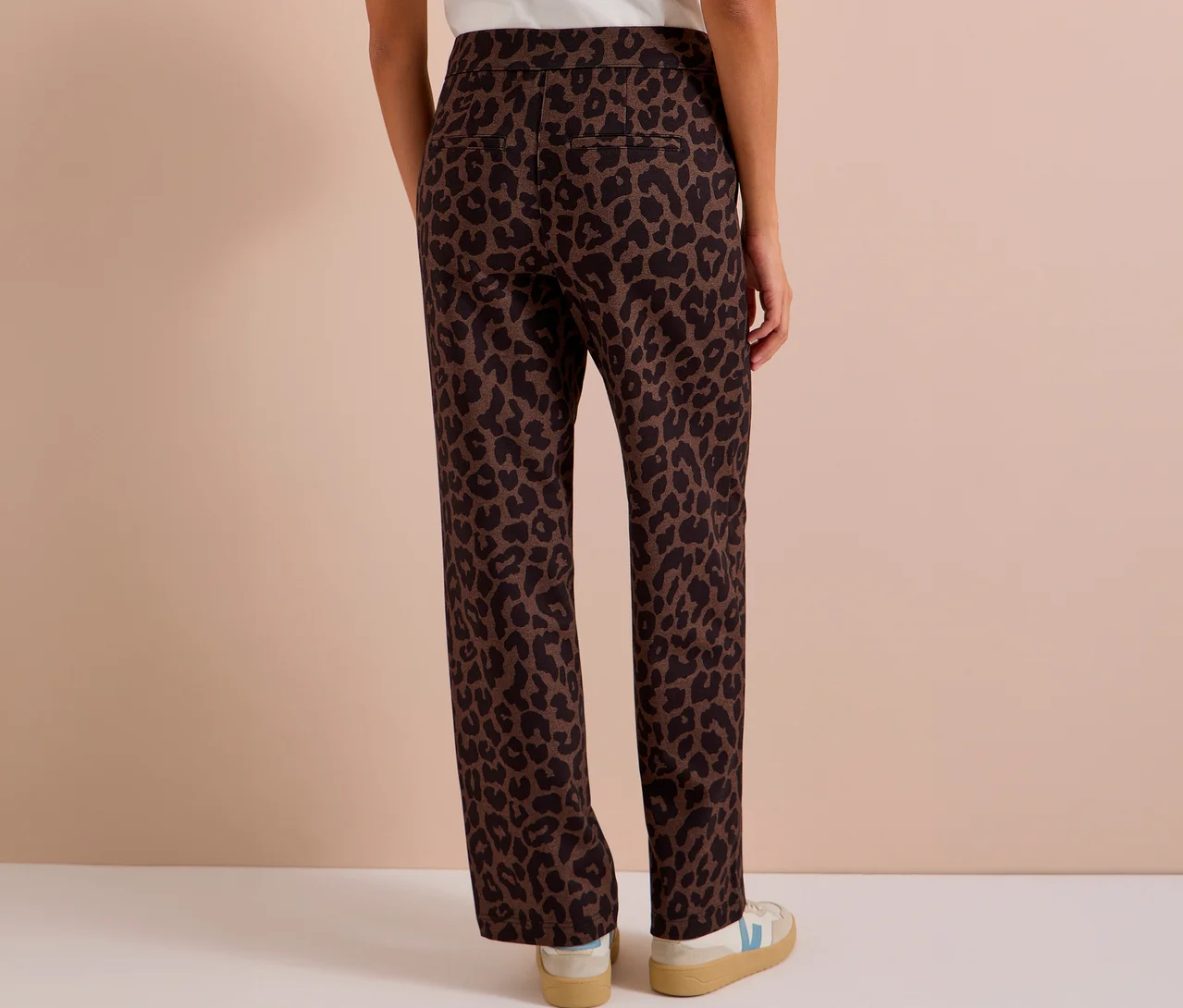 Eine Person von hinten, die eine braun-schwarze CECIL Stoffhose mit Alloverprint und weiss-beige Sneaker trägt.