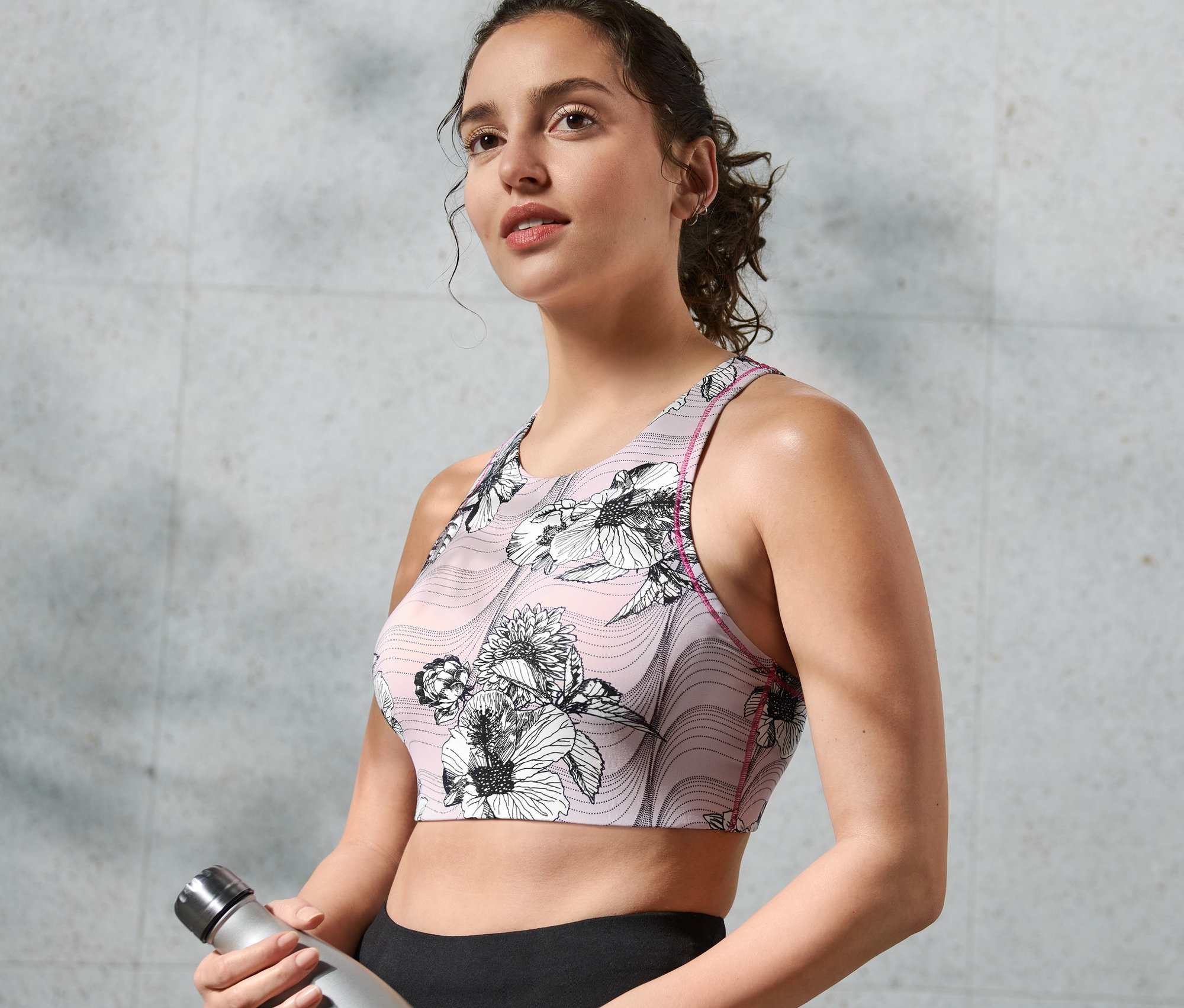 Frau hält eine Wasserflasche und trägt ein Sport-Bustier.