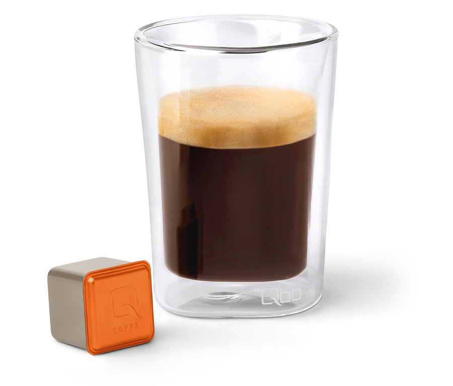 Ein Glas Qbo Caffè MINAS VERDE neben einer Kapsel.