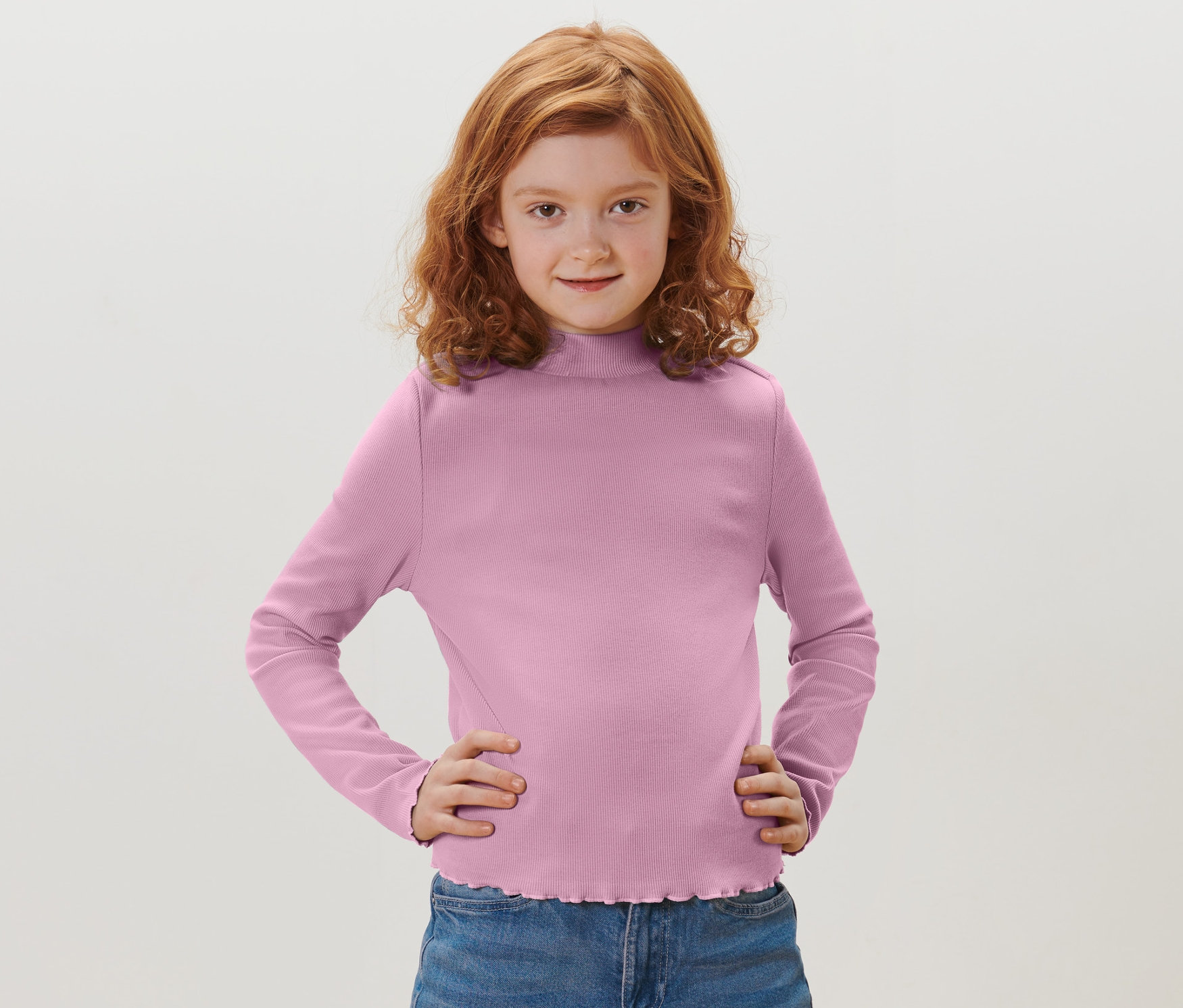 Mädchen mit roten Haaren posiert in einem violetten Kinder-Langarmshirt.