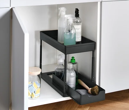 Ein offener, weißer Schrank mit einem höhenverstellbaren Schrankauszug, der Reinigungsmittel enthält.