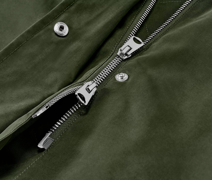 Detailansicht einer grünen Parka mit Kapuze, silbernem Reißverschluss und Druckknöpfen.