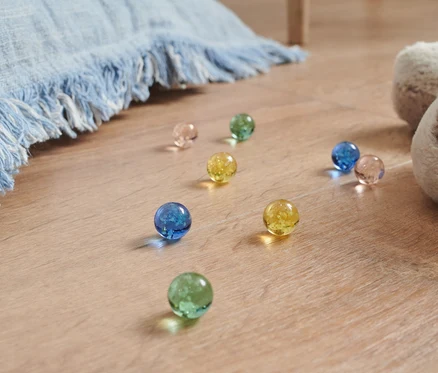 Leuchtmurmeln in verschiedenen Farben liegen auf dem Boden neben einem Plüschhund und einer blauen Decke.