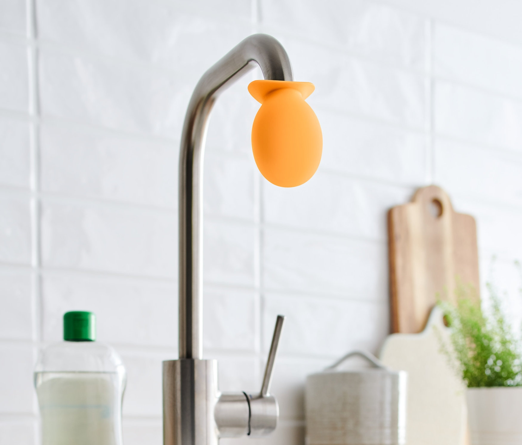 Auf einem Wasserhahn ist ein orangefarbener Wasserhahn-Entkalker-Aufsatz angebracht.