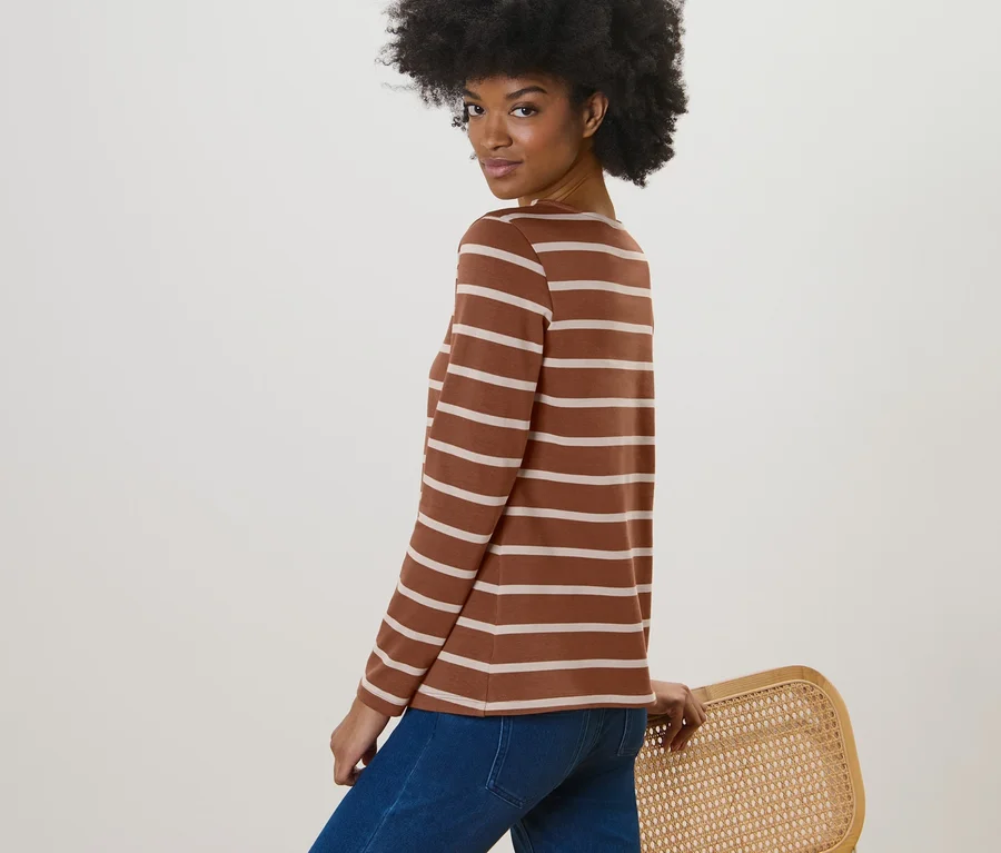 Frau posiert in einem gestreiften Langarmshirt in Cognac und blauen Jeans.