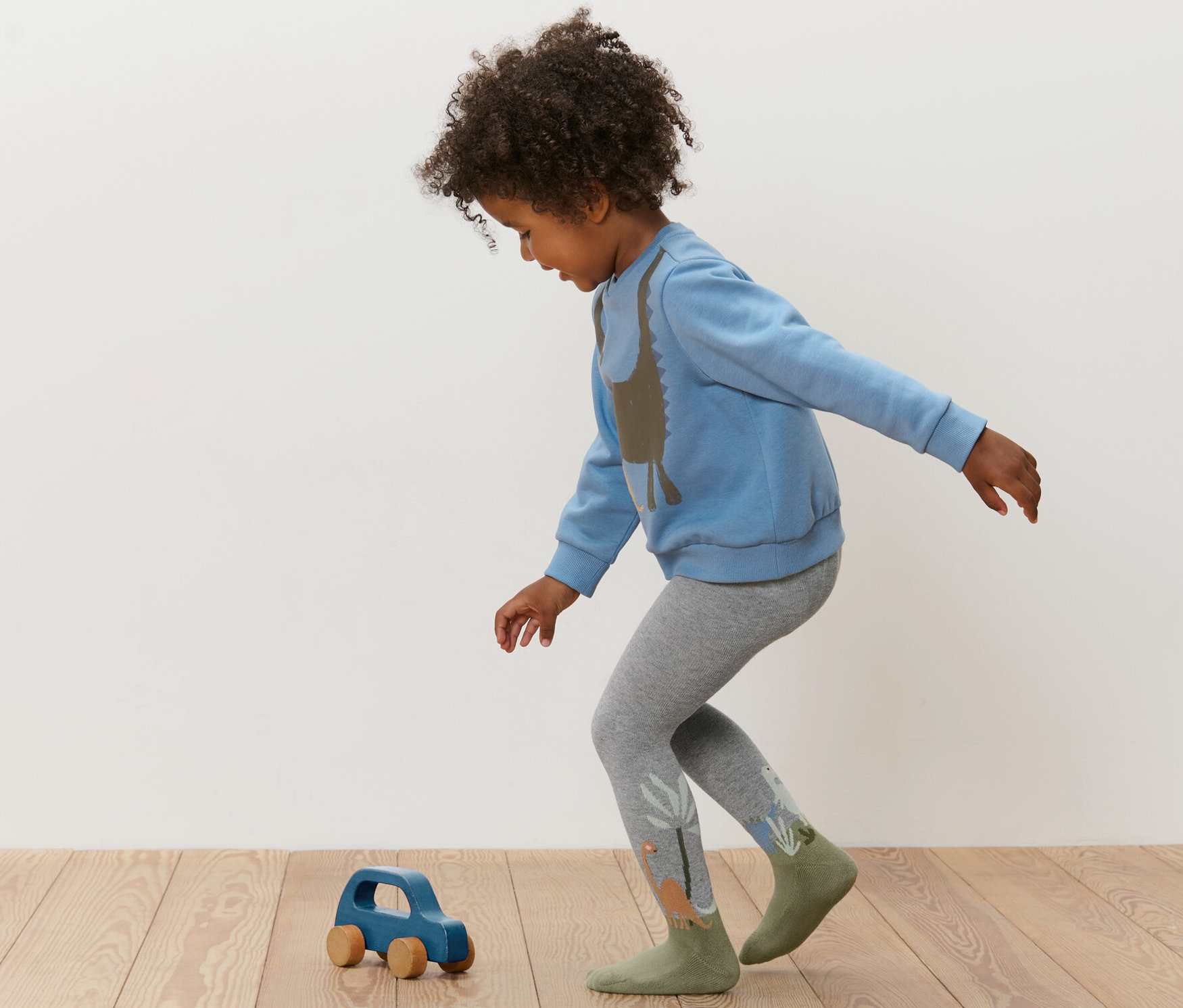 Ein Kind spielt mit einem blauen Holzauto und trägt einen blauen Pullover und graue Strumpfhosen. 3 Paar Kinder-Strumpfhosen, blau.