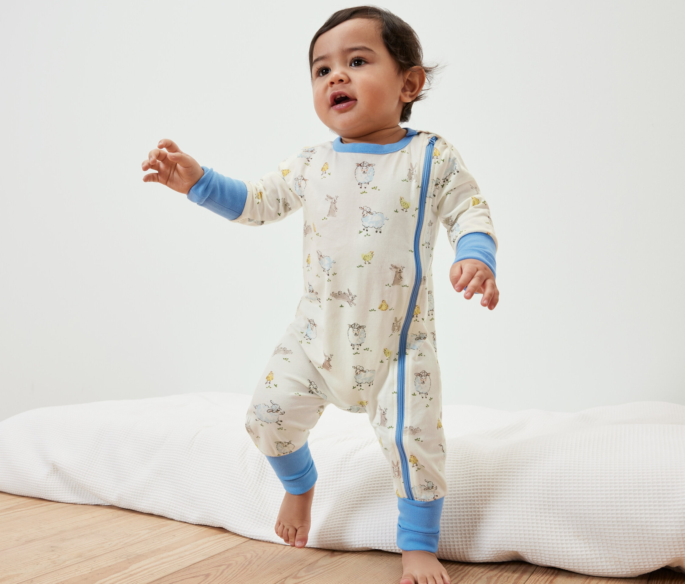 Kleinkind im Baby-Pyjama mit Tiermotiven steht auf einer Unterlage.