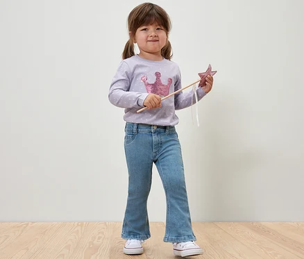 Lächelndes Mädchen hält Sternenstab und trägt Kinder-Jeans ‒ Fit »Emma«.
