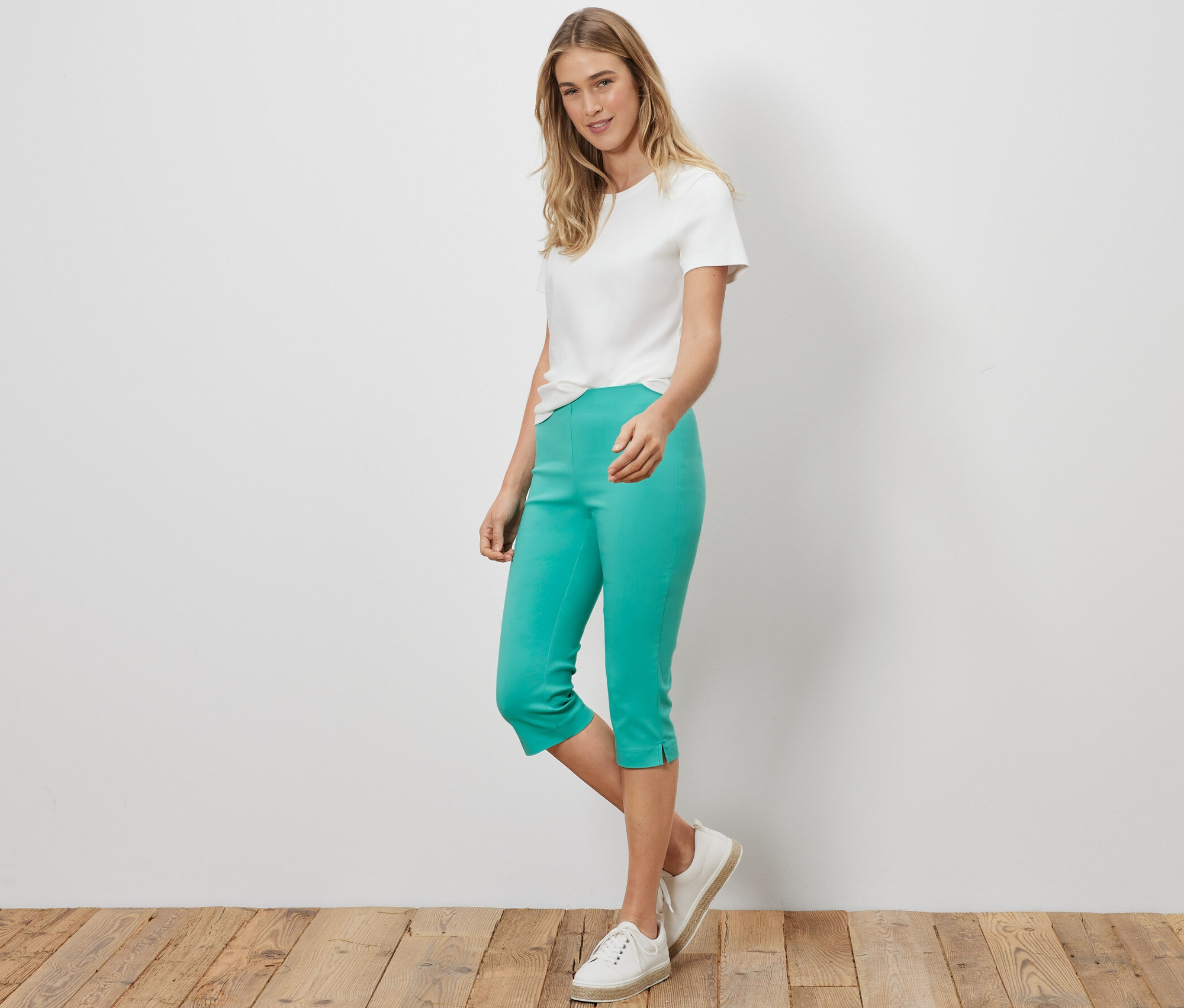 Frau steht und trägt ein weißes T-Shirt und eine türkise 3/4-Stretchhose.