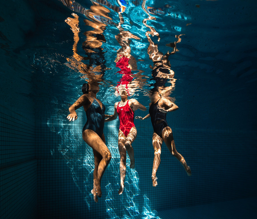 Drei Frauen schwimmen unter Wasser in einem Schwimmbecken. Eine der Frauen trägt einen arena Shapewear Damen Badeanzug Lara C-Cup.