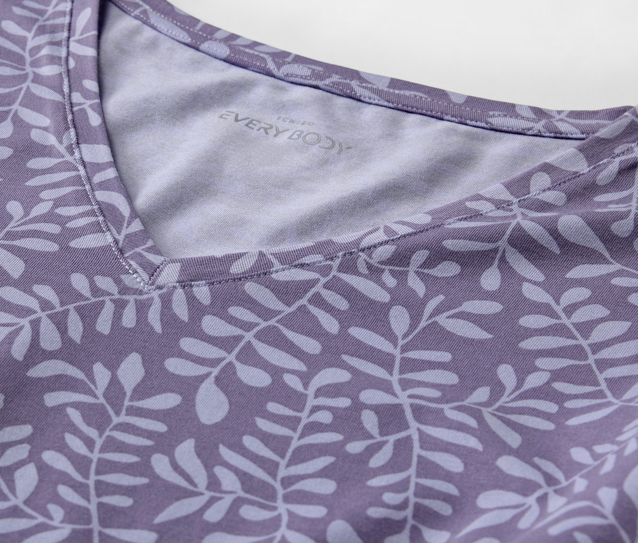 Detail eines lila T-Shirts mit Blätterdruck und V-Ausschnitt.