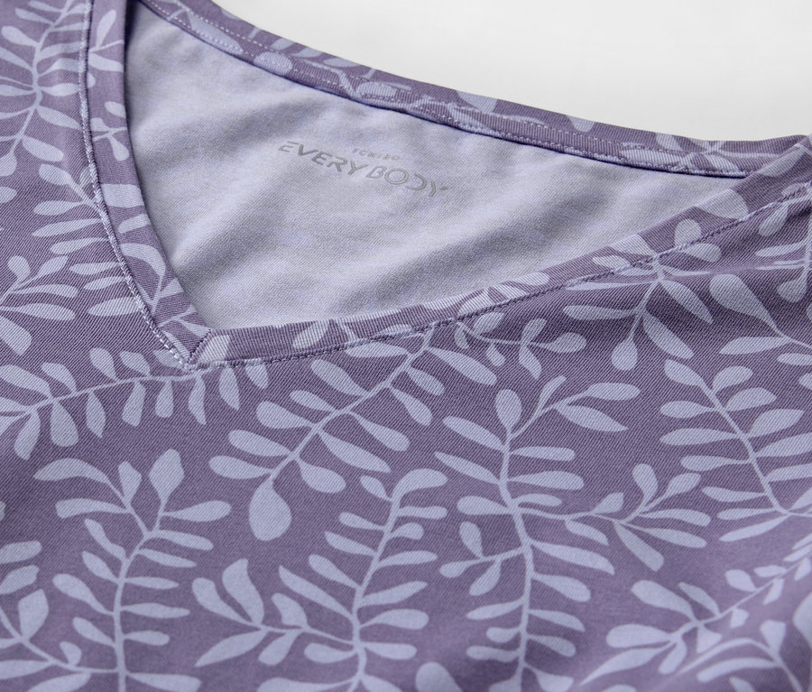 Detail eines lila T-Shirts mit Blätterdruck und V-Ausschnitt.