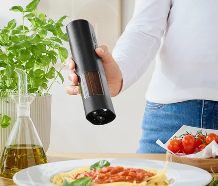 Frau würzt Spaghetti mit Tomatensoße mit einer Mühle. Auf dem Tisch stehen Basilikum, Olivenöl und Tomaten.