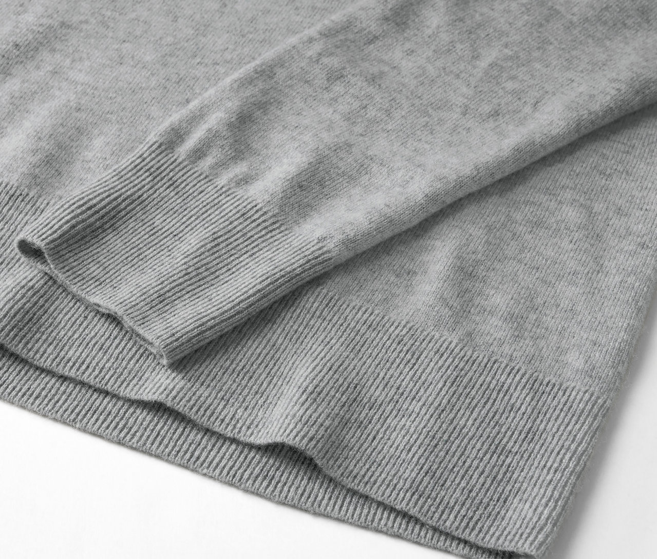 Detailansicht eines grauen Pullovers mit langen Ärmeln und geripptem Saum.