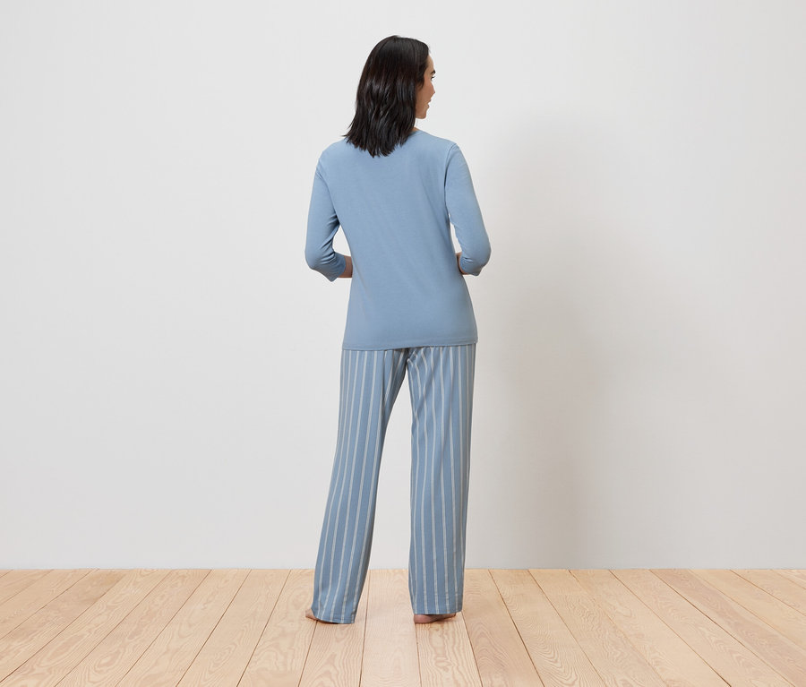 Frau in blauem Pyjama mit gestreiften Hosen, von hinten gesehen.