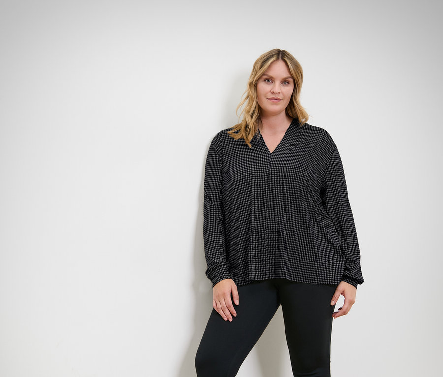 Frau posiert in einem schwarzen Oberteil und einer schwarzen Hose.