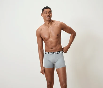 Lächelnder Mann posiert ohne Hemd und trägt graue Boxershorts mit Star Wars-Bund.