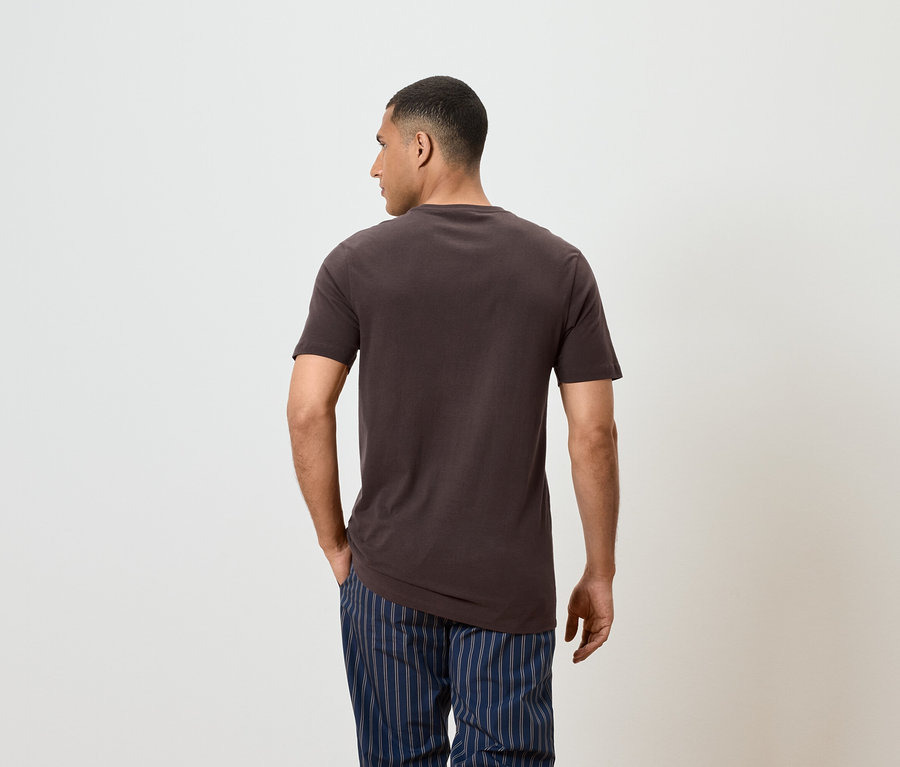 Mann von hinten trägt ein braunes T-Shirt und blau gestreifte Hosen.