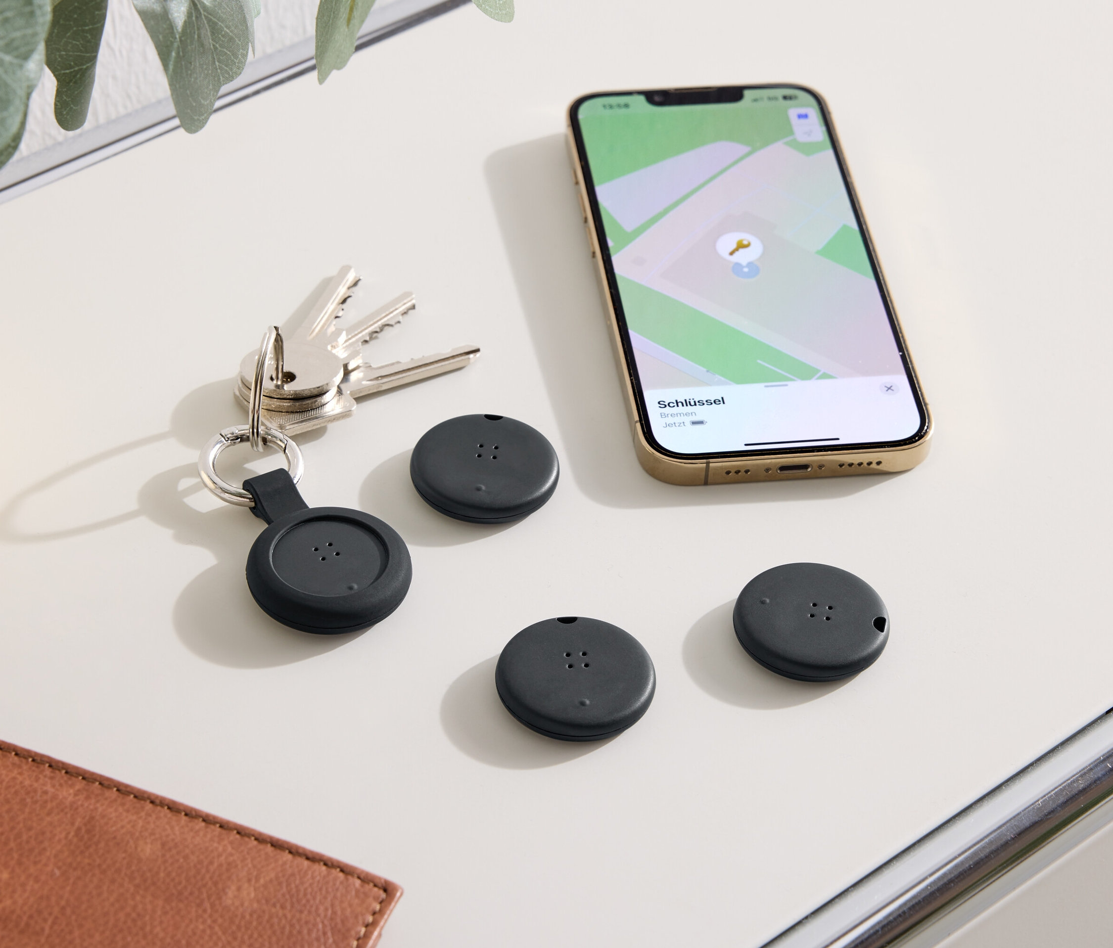 Auf einem Tisch liegen Schlüssel, ein Telefon mit einer Karten-App und drei schwarze Ortungsgeräte.