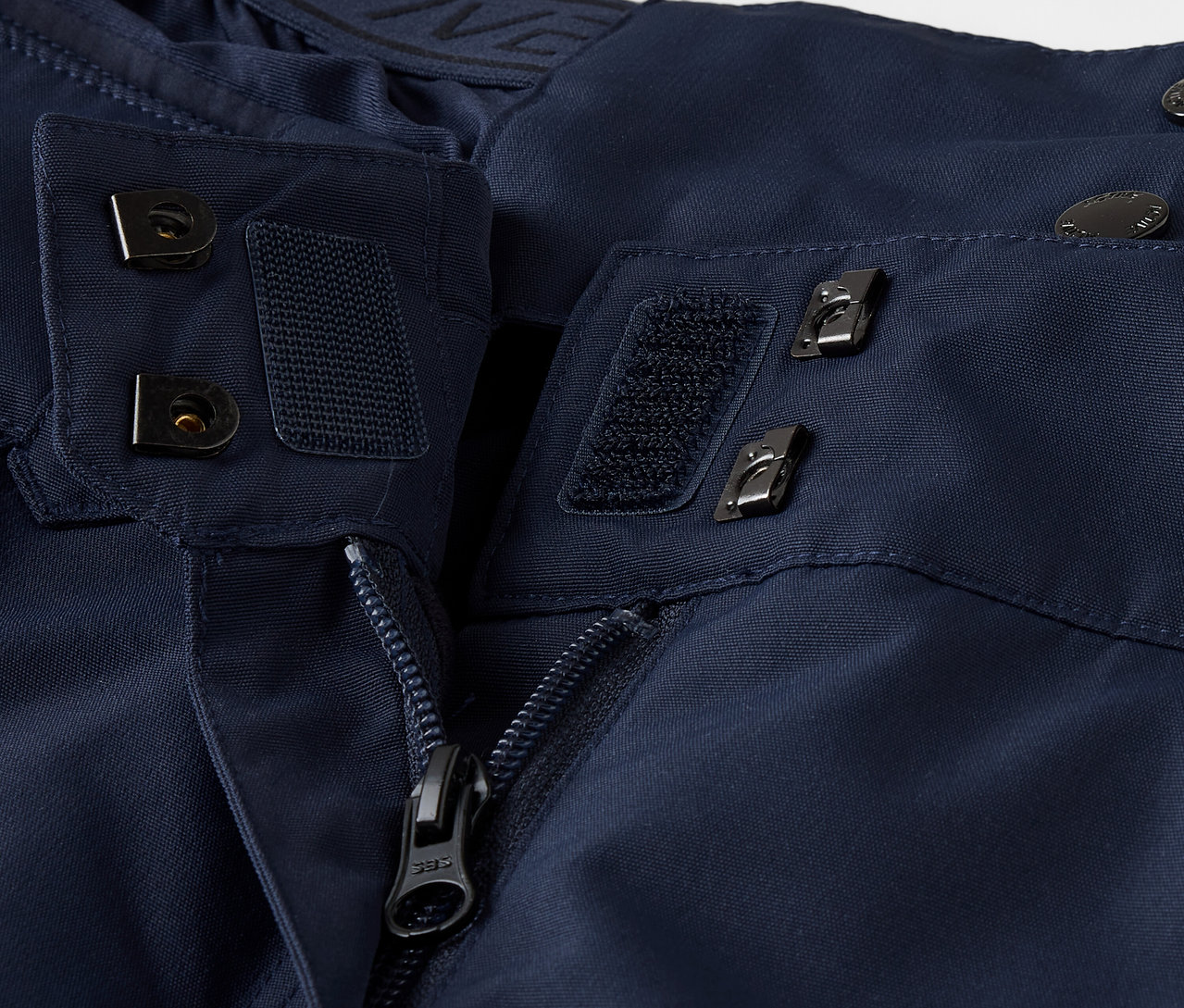 Detailaufnahme einer marineblauen Jacke mit Reißverschluss, Klettverschluss und Knöpfen.