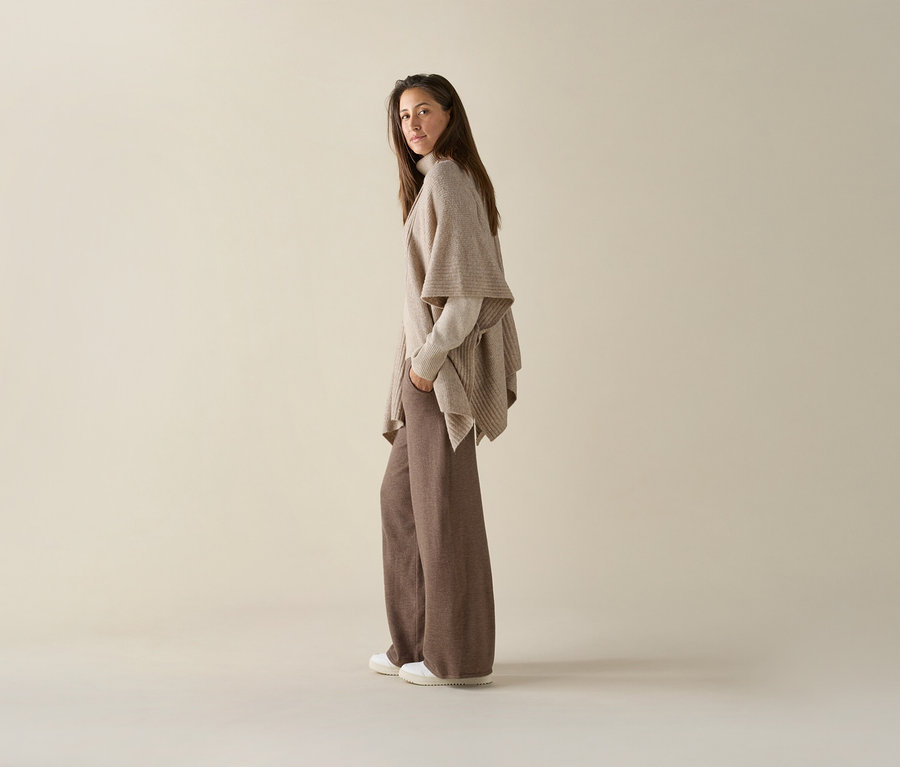 Frau posiert in brauner Schlaghose und beige Strickjacke mit weißen Tom Tailor Sneaker aus PU.