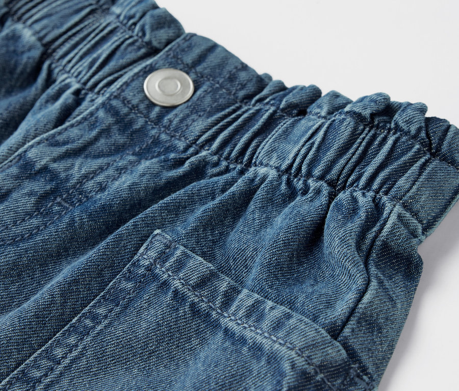 Detailaufnahme von Kinder-Jeansshorts mit elastischem Bund und Knopf.