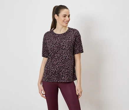Frau trägt ein violettes Leopardenmuster-T-Shirt und violette Leggings vor einem weißen Hintergrund.