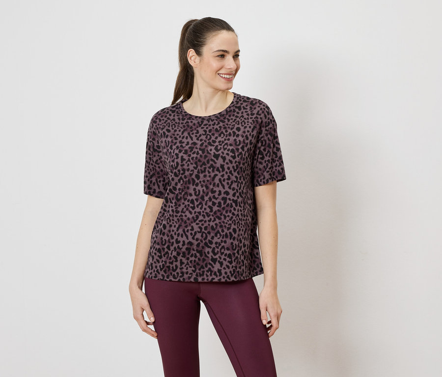 Frau trägt ein violettes Leopardenmuster-T-Shirt und violette Leggings vor einem weißen Hintergrund.