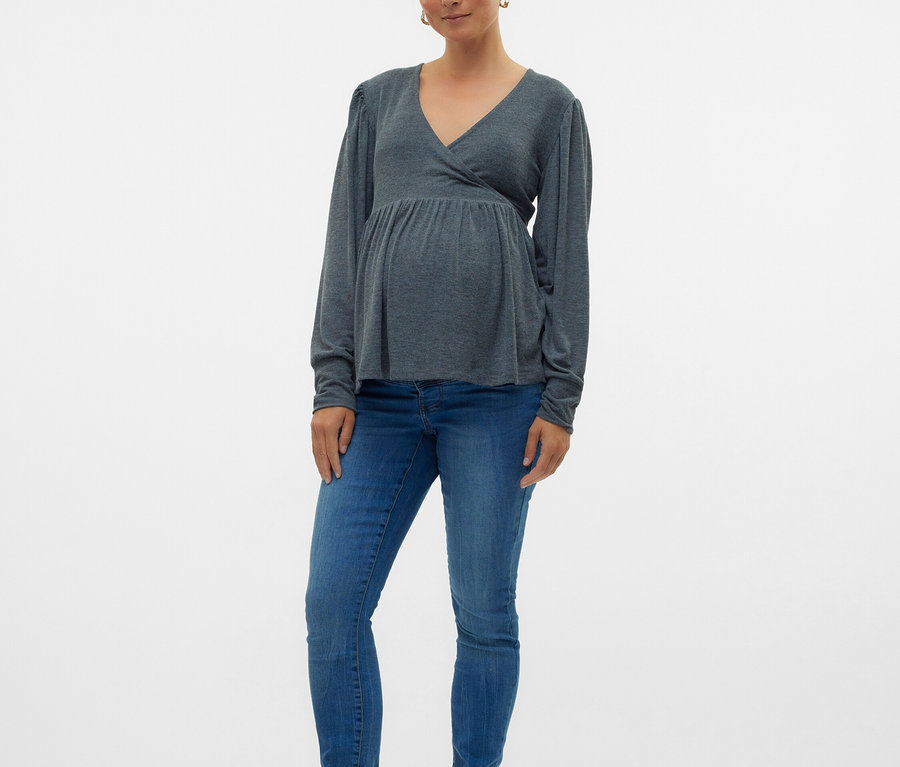 Schwangere Frau trägt ein graues Langarmshirt, blaue Jeans und schwarze Ballerinas.