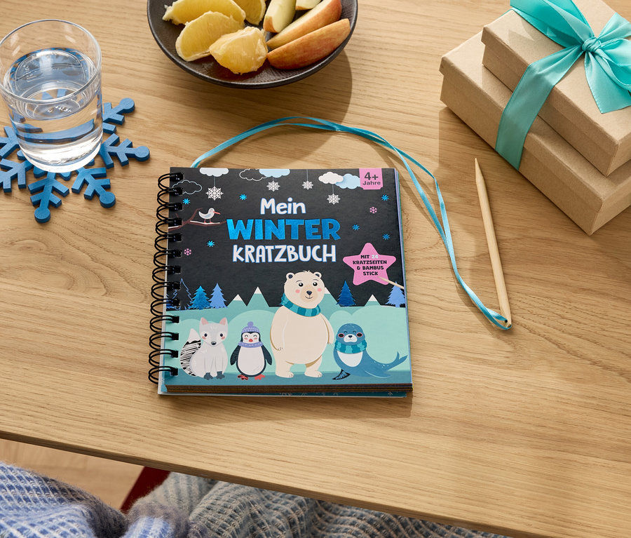 Ein Tisch mit einem Glas Wasser auf einem blauen Schneeflockenuntersetzer, einem Teller mit Apfel- und Orangenscheiben, zwei Geschenkboxen mit blauem Band und einem Winter-Malbuch.