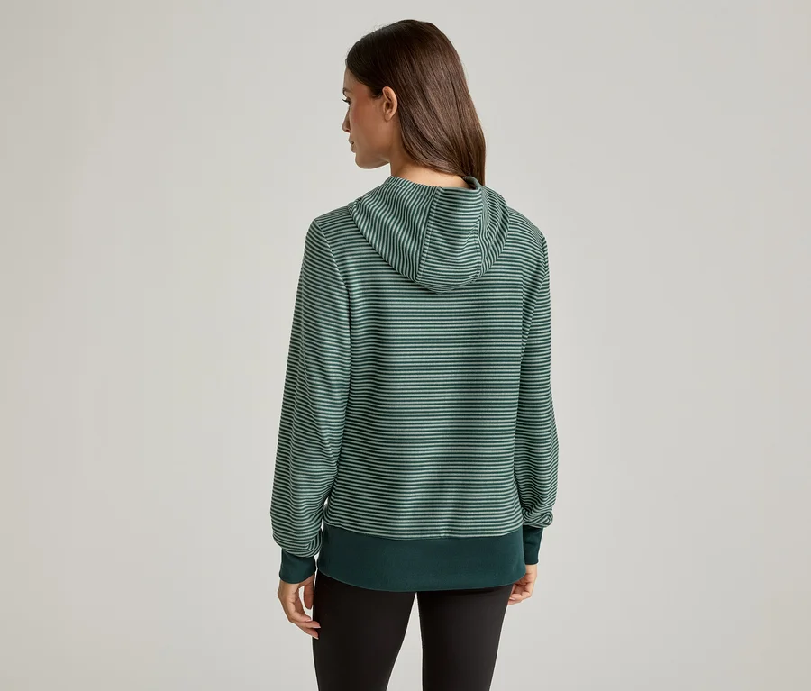 Rückansicht einer Frau mit braunen Haaren, die einen grün gestreiften Kapuzenpullover und schwarze Leggings trägt.