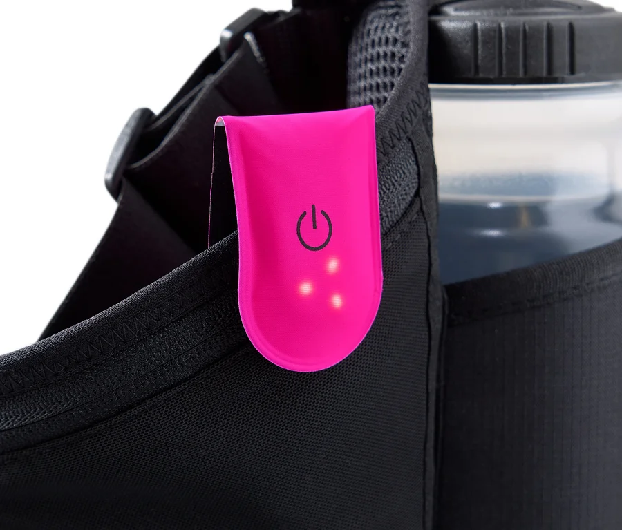 Nahaufnahme eines schwarzen Laufgürtels, an dem eine pinkfarbene Clip-Leuchte mit Einschaltsymbol und drei leuchtenden Punkten befestigt ist. Eine Wasserflasche steckt in einer Netztasche.